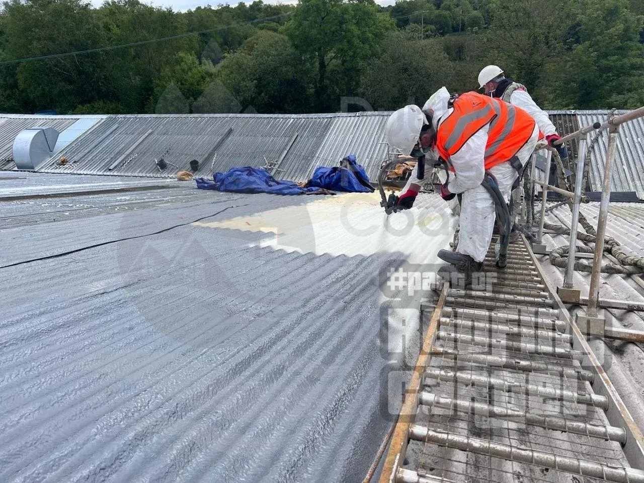 **Application of Polyurea Membrane:** Professional spray application of polyurea coating onto prepared asbestos substrate, demonstrating the seamless waterproofing system installation. This middle layer creates exceptional flexibility and durability whilst bonding permanently to the asbestos surface. Industrial asbestos roof encapsulation with Polyurea spray coating in Dublin Ireland